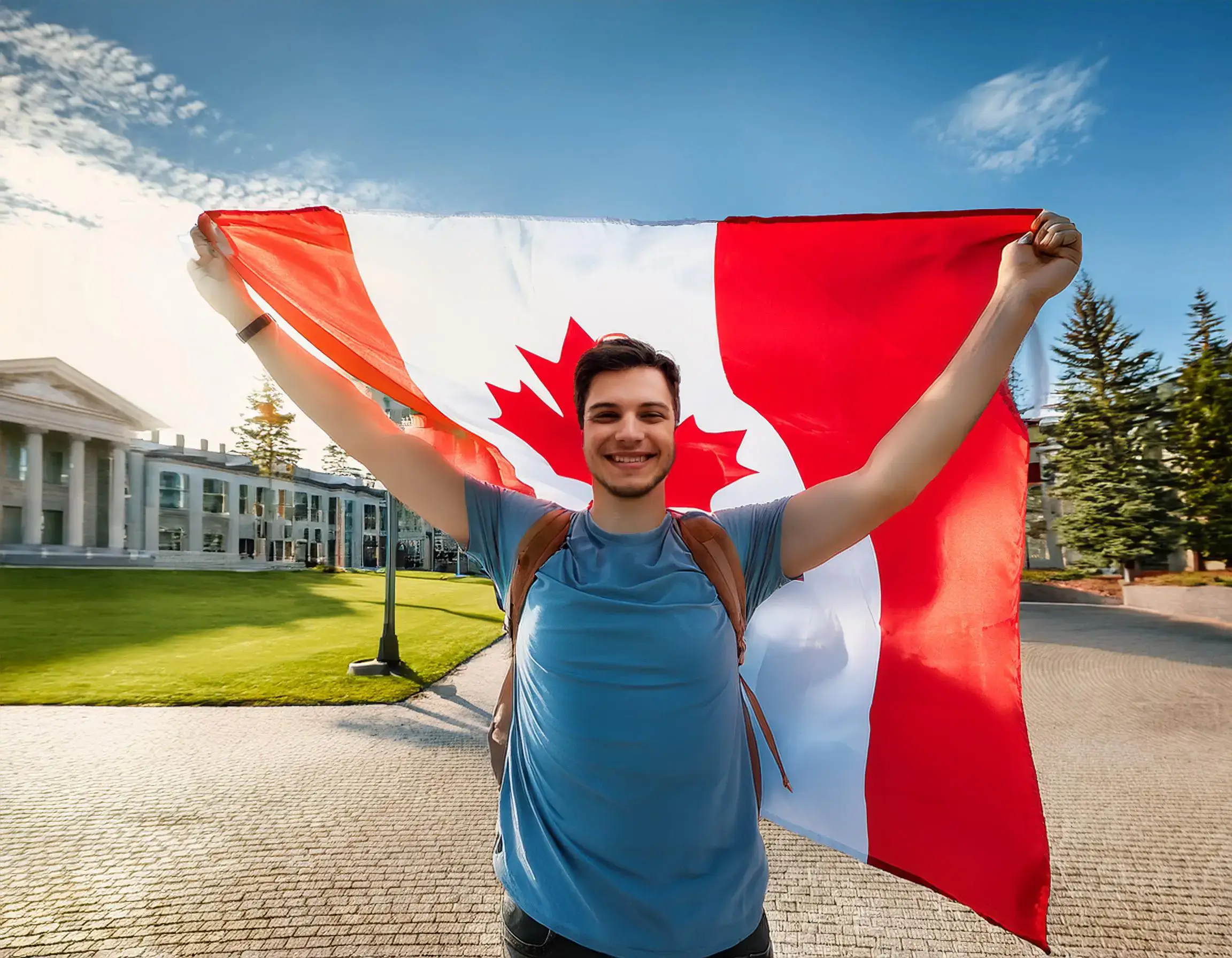 A person stands on a paved path, beaming as they hold a Canadian flag overhead, celebrating their Canada immigration. Dressed in a blue shirt and backpack, they stand amidst grassy spaces, trees, and a building under the clear blue sky.